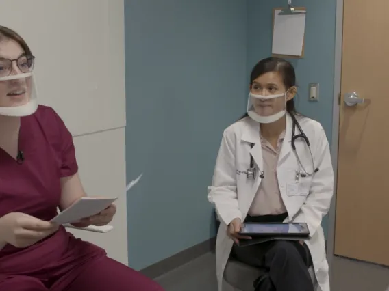 Image of two young healthcare professionals speaking to an young man with a disability.