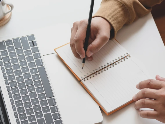 Overhead image of a pair of hands taking notes in front of a laptop