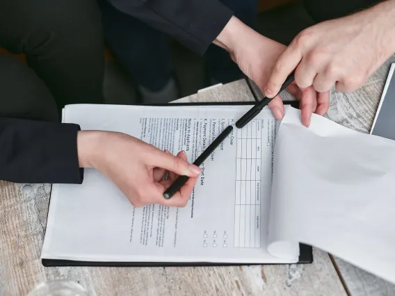 2 people's hands holding black pens reviewing a health policy contract