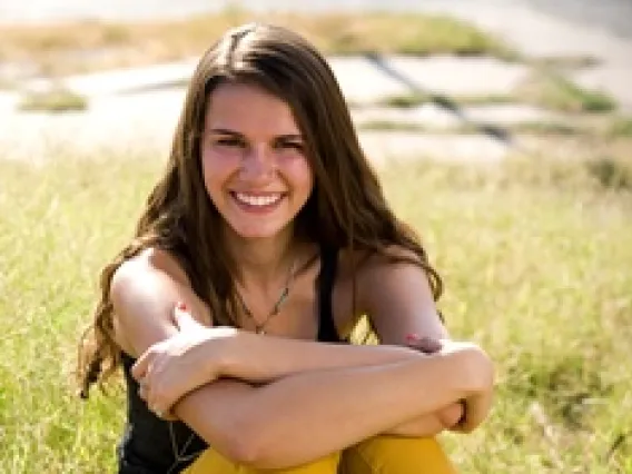 Jasmine, a girl with long hair sitting on grass smiling