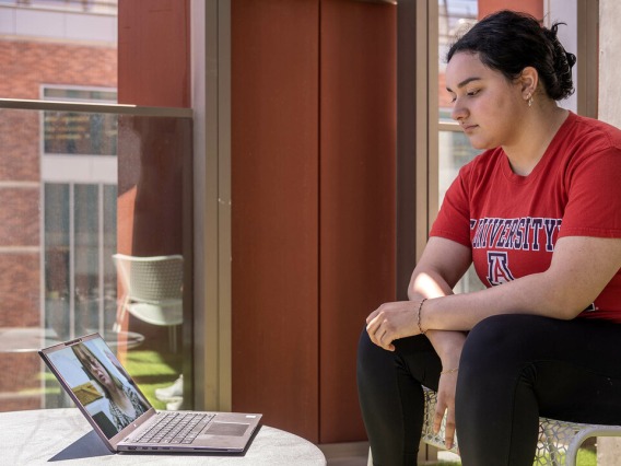 A woman wearing red UA top sitting next to a laptop