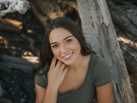 Woman with brunette hair, wearing a dark green shirt looking up at camera smiling