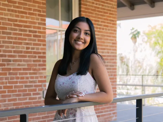 Woman wearing a white dress, smiling at camera. She has long black hair 