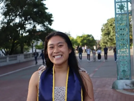 Cosette Tsai, a person with long brown hair, smiling, outside, wearing a floral top with blue and yellow graduation cords