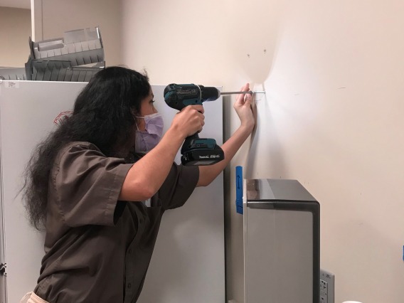 woman with black long hair using an electronic screwdriver against an office wall