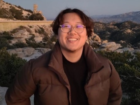 Andrew Leung,  young person with medium length brown hair and glasses standing outside on a clear evening at sunset