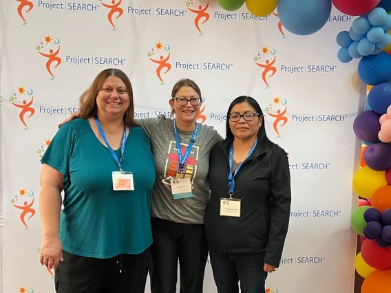 Three women posing for a photo in front of a Project SEARCH step-and-repeat banner.