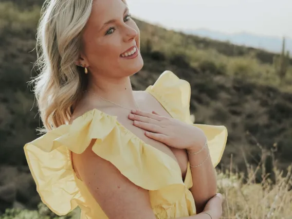 Photo of a woman wearing a yellow flowy dress with blonde shoulder length hair smiling 