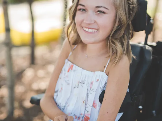 Woman in her power wheelchair with blonde hair wearing a white shirt smiling at the camera