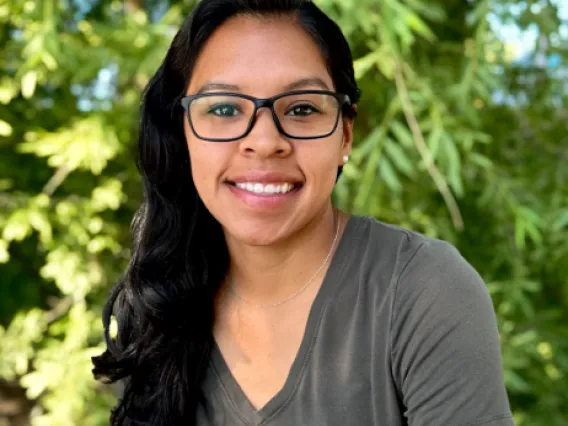 Headshot of Kelsey Montano, a hispanic woman with long dark hair, wearing glasses and a grey vneck tshirt.