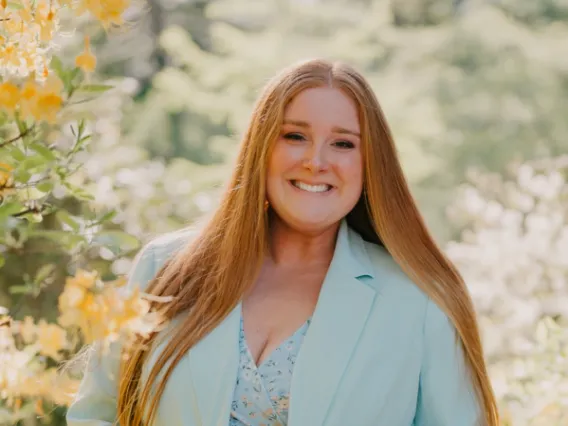 Portrait of Makenna Thuringer, a white woman with long straight red hair, wearing a powder blue blazer.