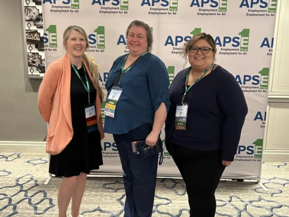 Jessica Winchester (left) and Rosa Rojas Franco (right) pose in front of a banner with the logo of the APSE Employment First, Employment for All Conference. 