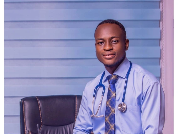 headshot of young man wearing a blue collard shirt, checkered tie, and with a stethoscope around his neck