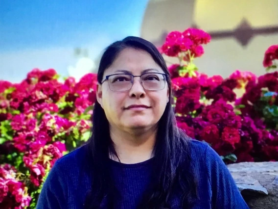 woman with long black hair, wearing glasses and is smiling at the camera