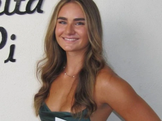 woman with long brunette hair is wearing a green dress and is smiling at the camera