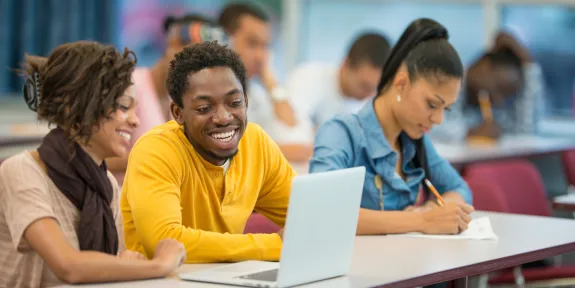 Image of three young Black students sitting in a lecture hall, smiling.