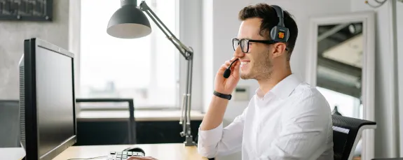 A Smiling Man Wearing a Headset Looking at His Computer Screen