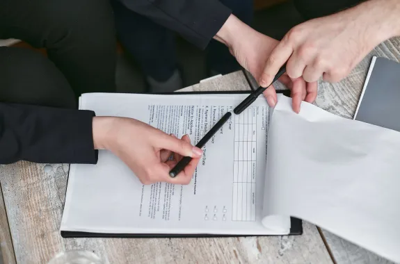 2 people's hands holding black pens reviewing a health policy contract