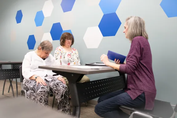 Three older adults sitting around a table in a classroom setting