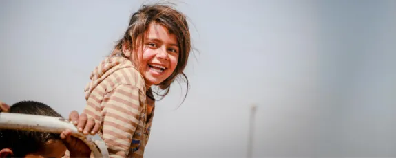 Young refugee girl smiling while her hair blows in the wind.