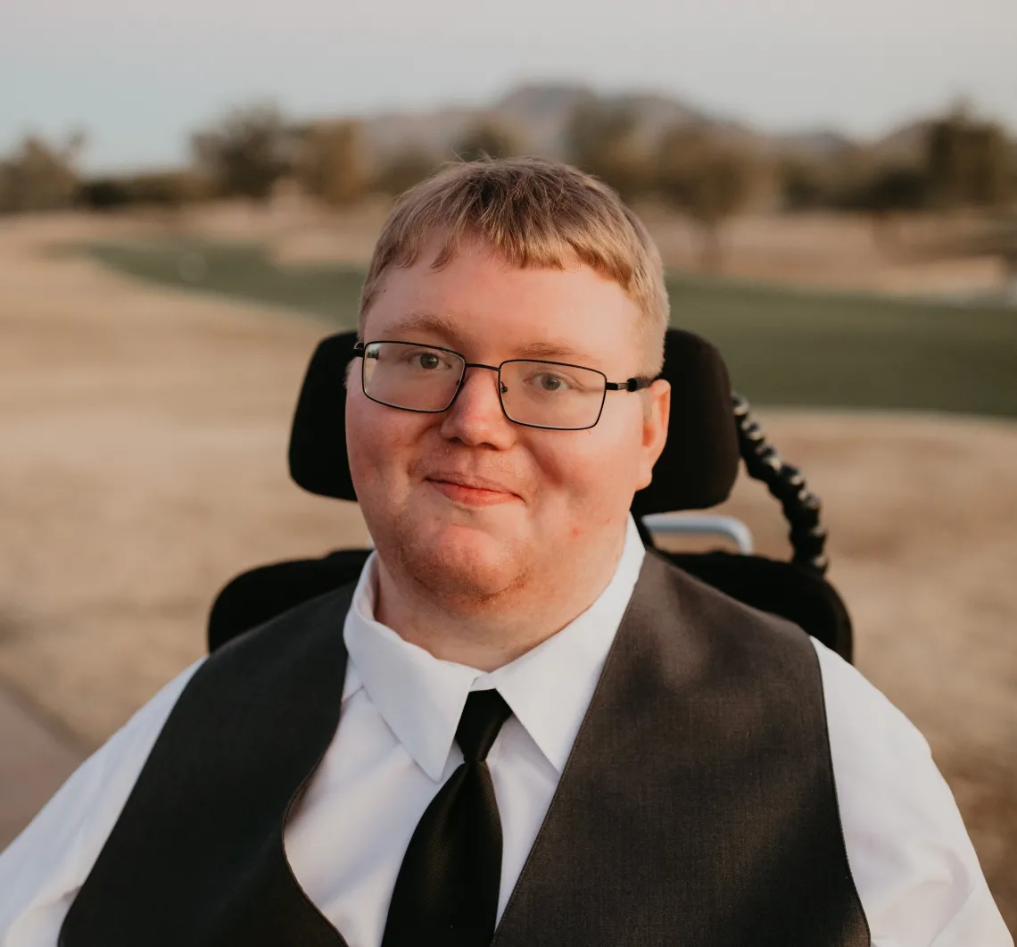 White man with glasses wearing a suit vest and tie, sitting in a wheelchair