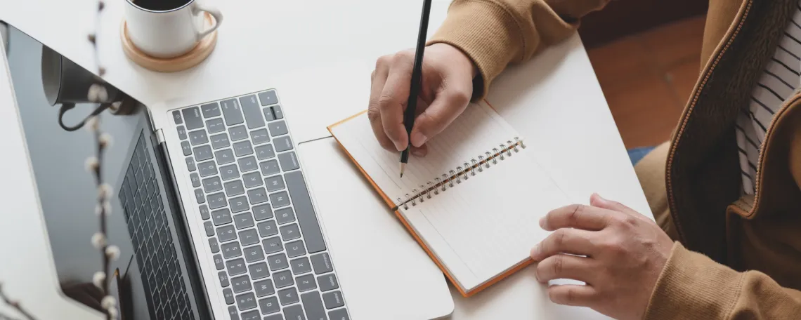 Overhead image of a pair of hands taking notes in front of a laptop