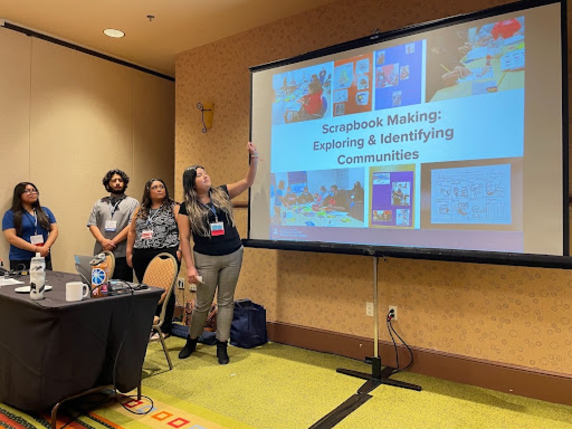 Four people standing to the left of a presentation screen that displays a slide saying "Scrapbook Making:  Exploring and Identifying Communities"