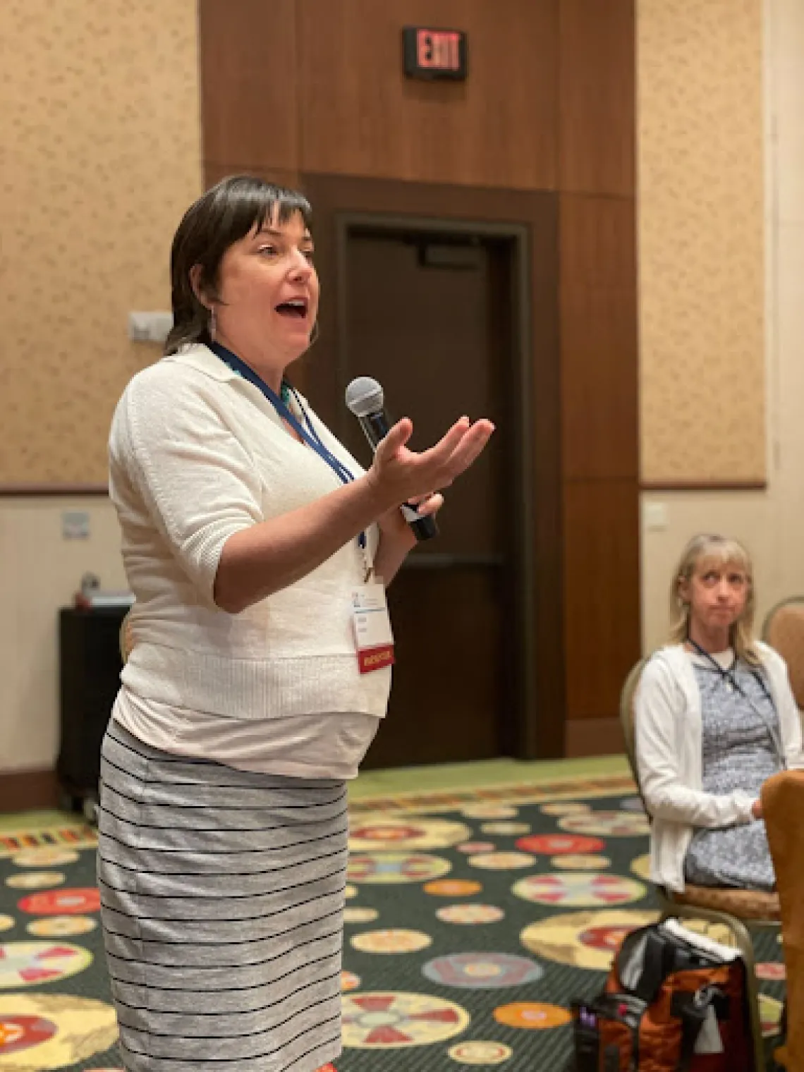 White woman with short dark hair wearing a white sweater, speaking into a microphone