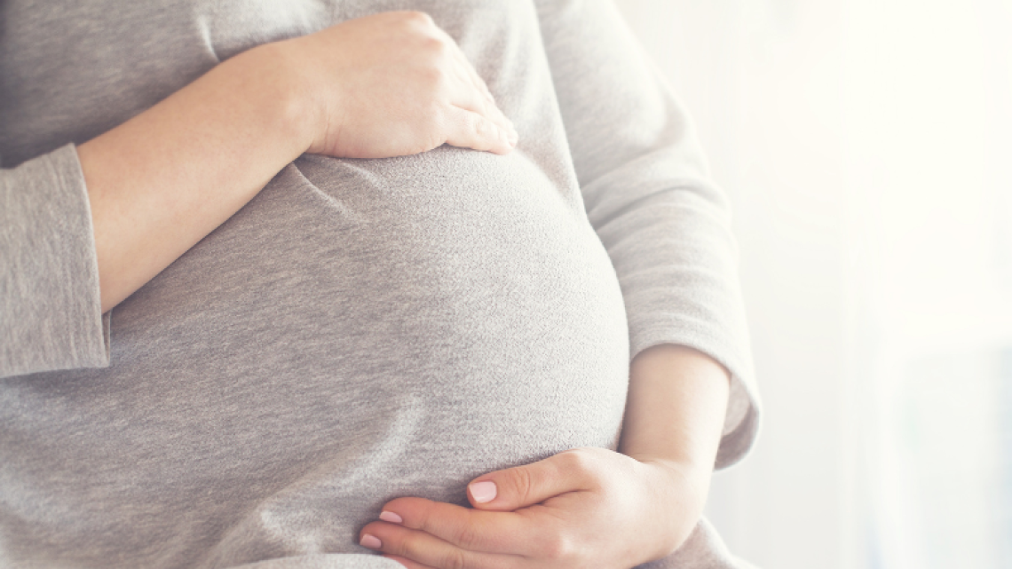 Close-up image of pregnant woman holding her stomach with both hands