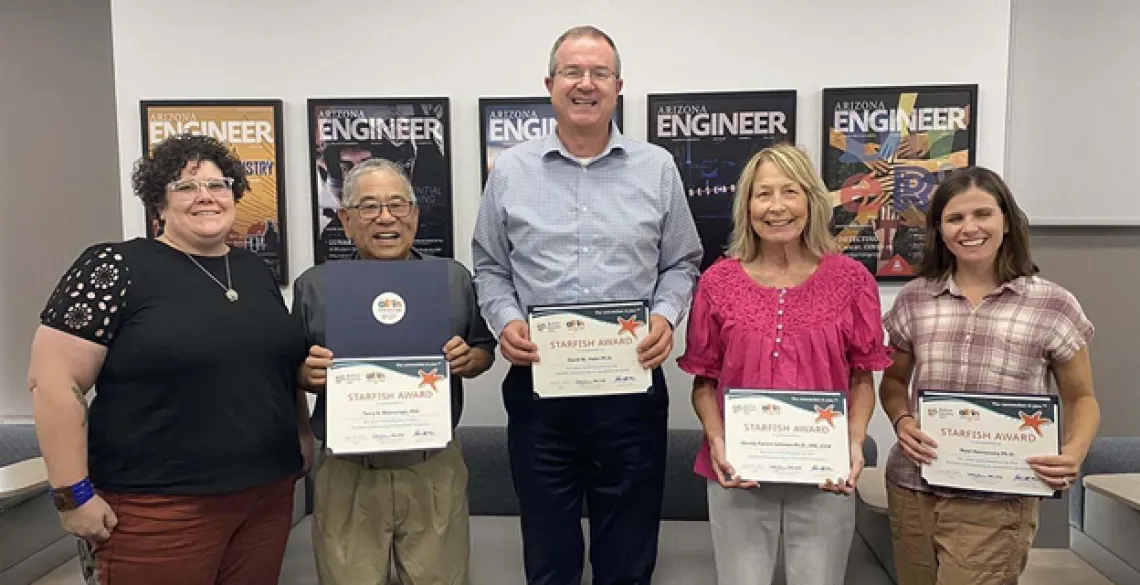 Five people standing in a row, each holding a certificate in front of them.