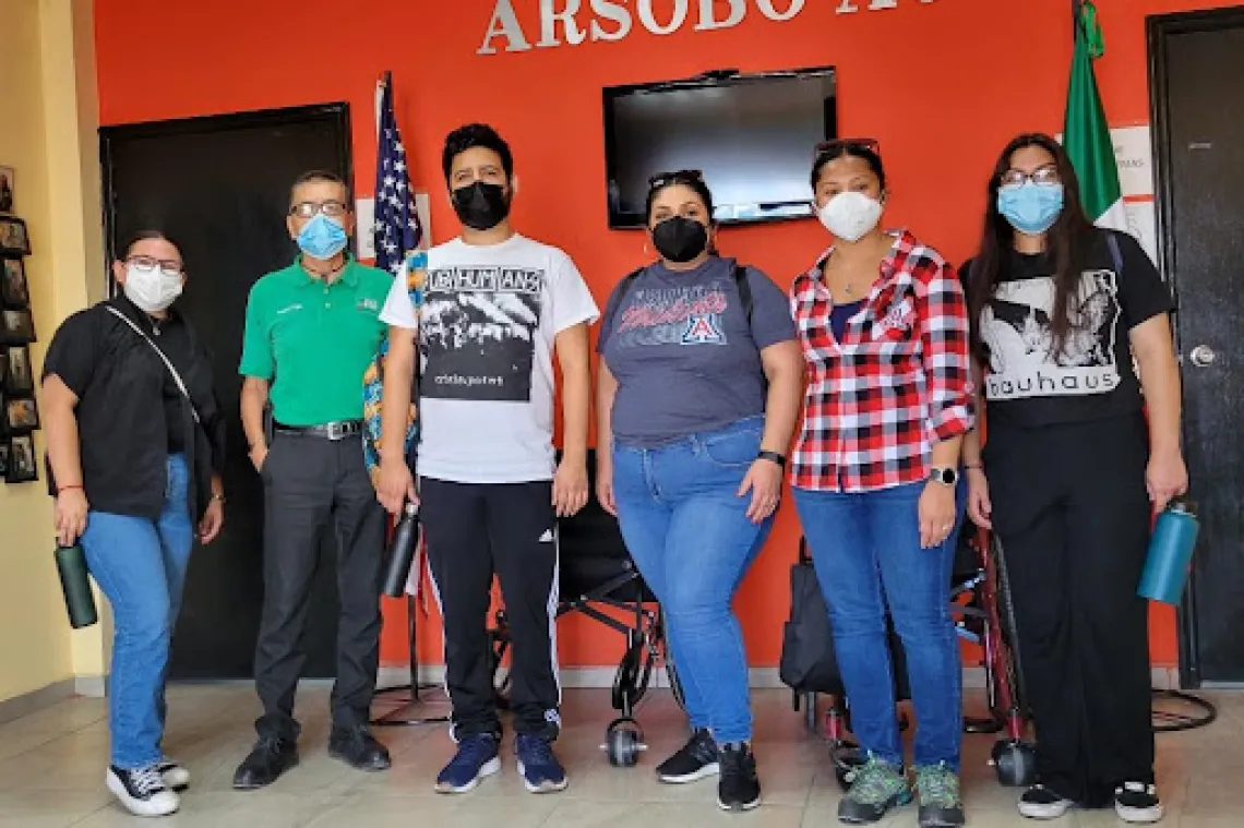  Fellows are posing alongside ARSOBO Executive Director, Kiko Trujillo and Sonoran Center for Excellence in Disabilities staff, Celina Urquidez and Jacy Farkas. Left to right: Paulette Nevarez is wearing a black shirt with a black button up over with blue jeans and black shoes, Kiko Trujillo is wearing a green polo with black pants and black shoes, Abraham Venegas is wearing a white shirt with a graphic with black pants and black shoes, Celina Urquidez is wearing a gray shirt with the A for UA