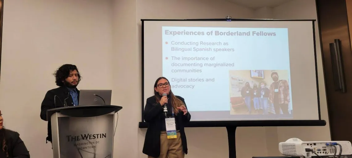 Abraham Venegas stands at a podium and Paulette Nevarez stands next to him with a microphone as they give their presentation on the DISCAPAZ project. 