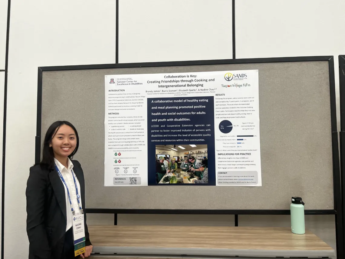 Nadine Chau, wearing a black jacket and white shirt, standing in front of her posterboard presentation.