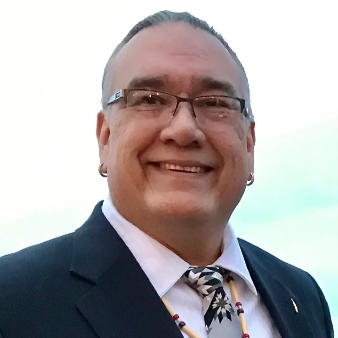 Jim Warne, a Native American man wearing a black jacket, white shirt, and brown tie