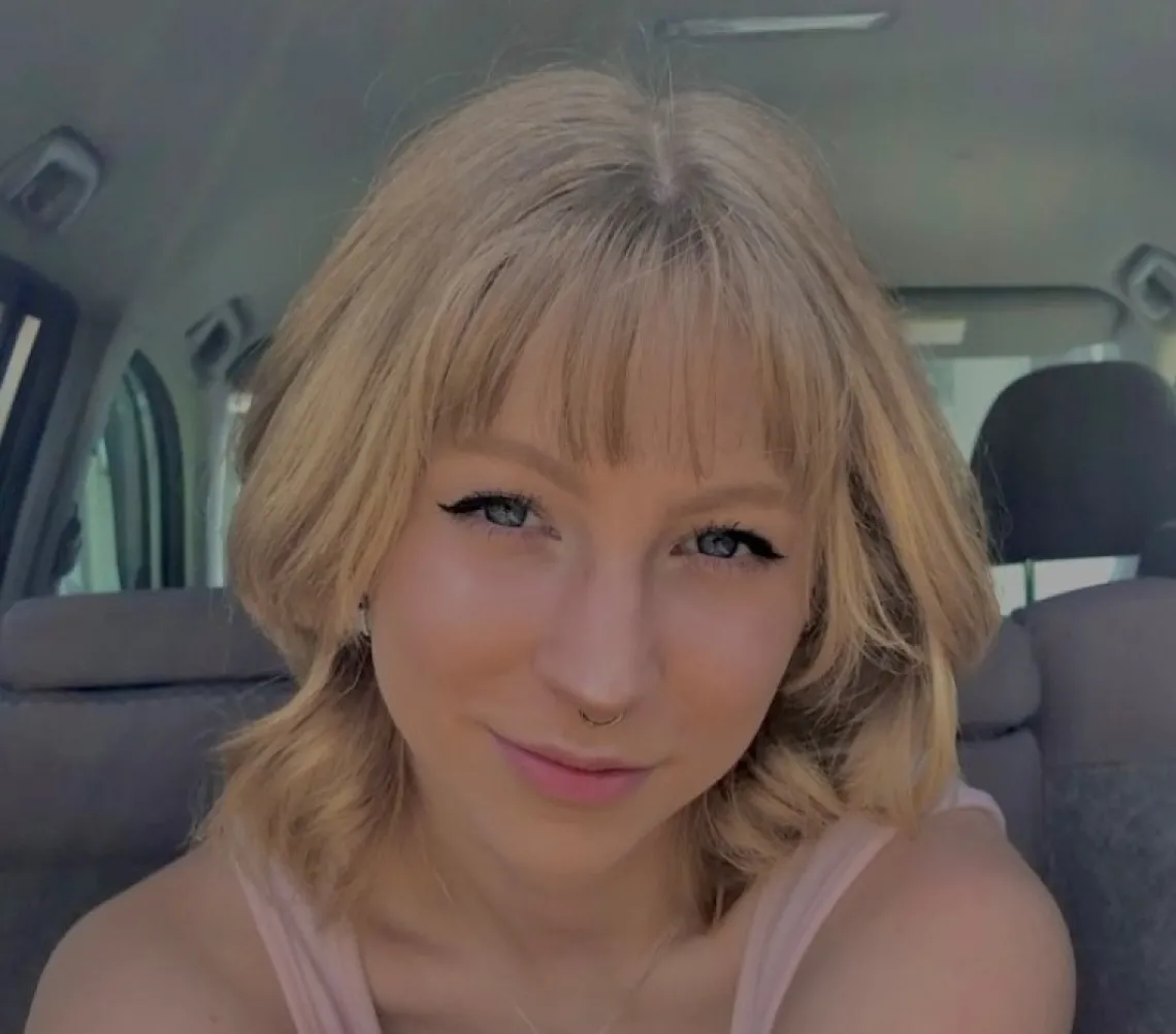 Amber Chase, a young woman with blonde hair, sitting in a car with a slight smile