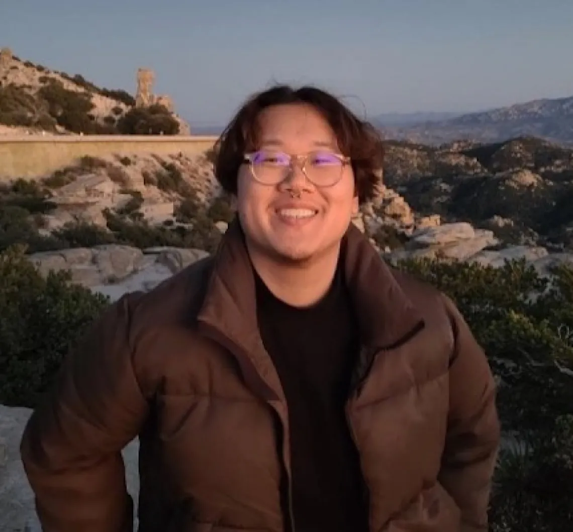 Andrew Leung,  young person with medium length brown hair and glasses standing outside on a clear evening at sunset