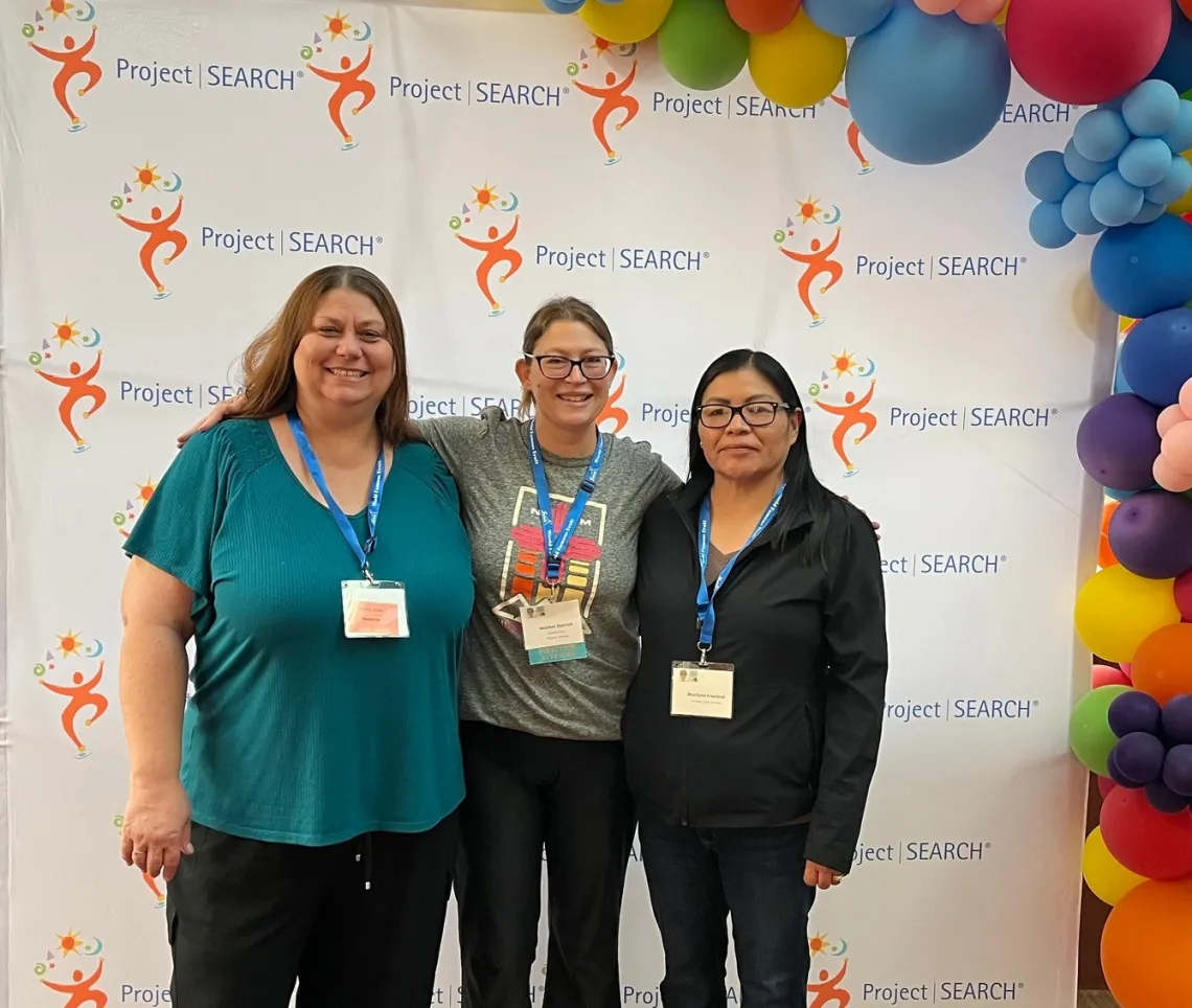 Three women posing for a photo in front of a Project SEARCH step-and-repeat banner.