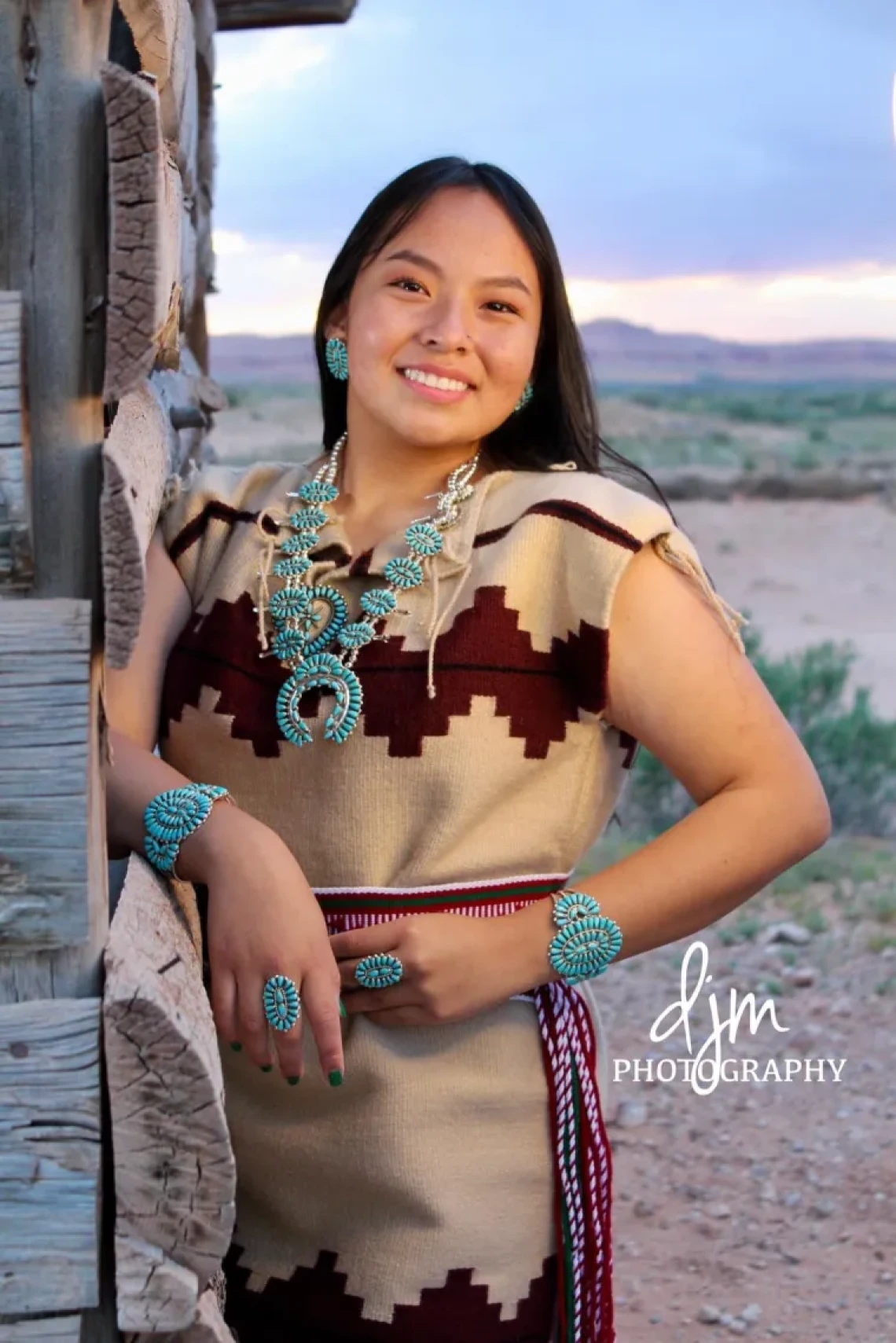 Alanna Begay, a young person with long brown hair, standing outside, wearing a brown dress and smiling