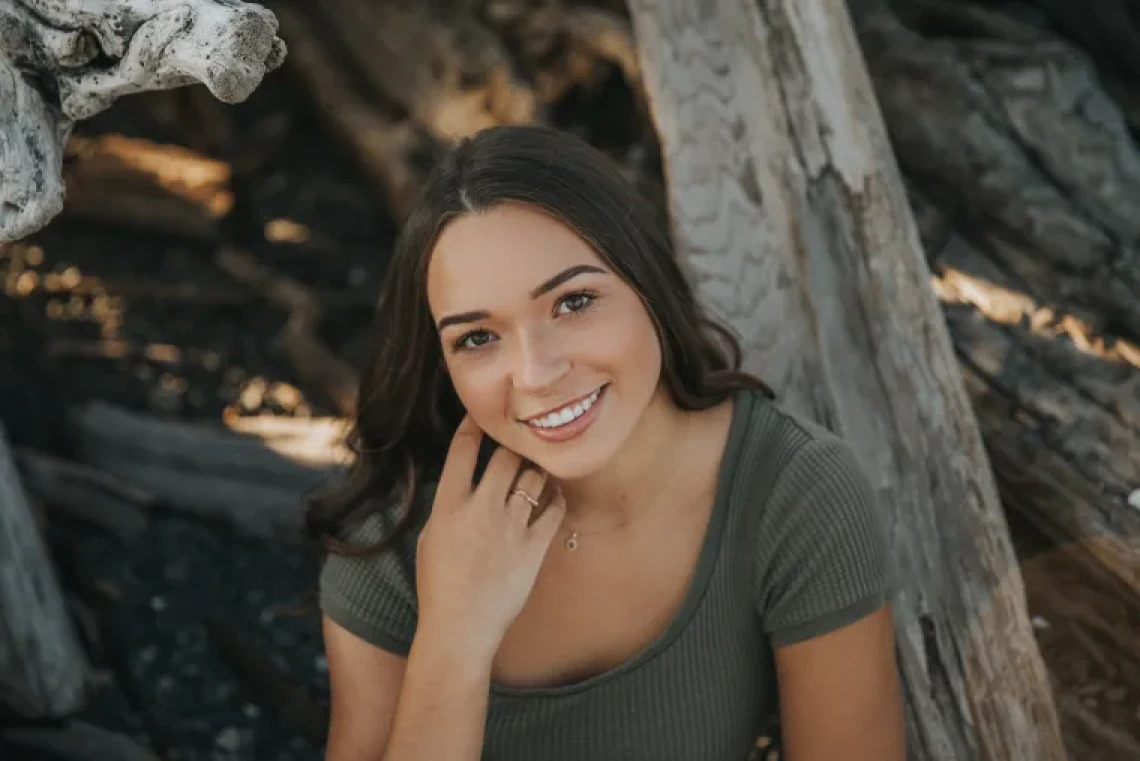 Alexia Tawrel, a young woman sitting outside in a wooded area, looking up at the camera and smiling