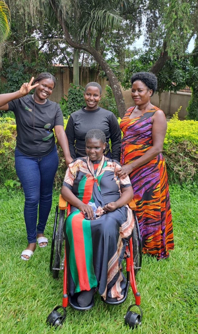 Three women standing behind another woman seated in a wheelchair.
