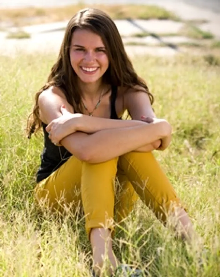 Jasmine, a girl with long hair sitting on grass smiling