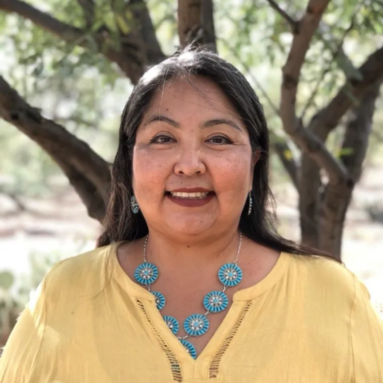 Native woman with long dark hair wearing a yellow blouse and turquoise necklace