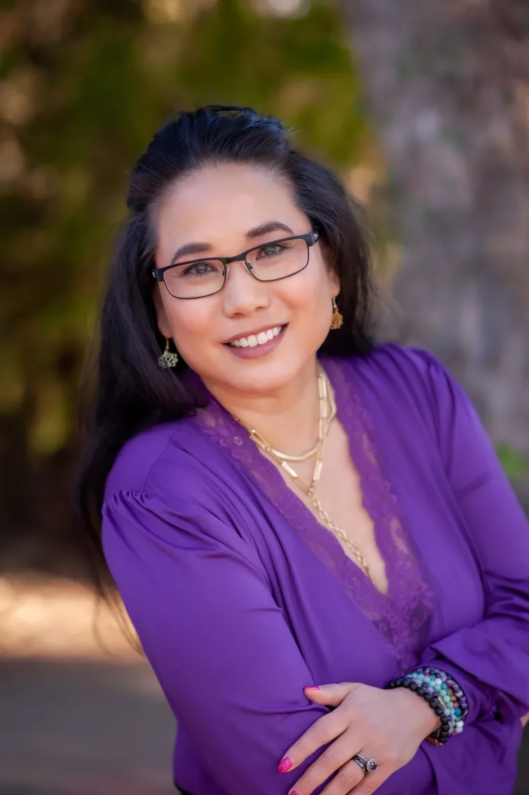 Woman with long dark hair and glasses wearing a purple blouse