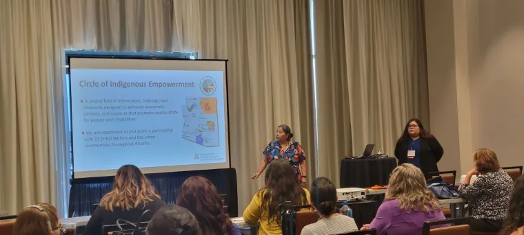 Agnes Attakai (left) and Rosa Rojas-Franco (right) present on the Circle of Indigenous Empowerment. Agnes gesturing to a powerpoint slide in front of a crowd of attendees. The slide reads, "Circle of Indigenous Empowerment".