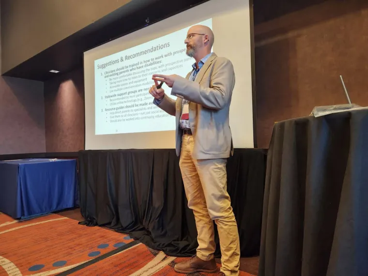 Austin Duncan presents about the Sonoran Center's project for pregnancy and parenting support for people with disabilities. Austin is gesturing in front of a projector with a powerpoint slide which reads "Suggestions and Recommendations".