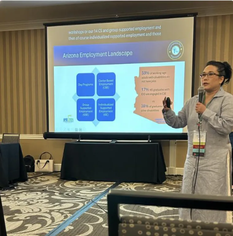 Lorie Sandaine describes the Arizona Employment Landscape at the APSE conference. She is gesturing in front of a powerpoint slide which reads "Arizona Employment Landscape".