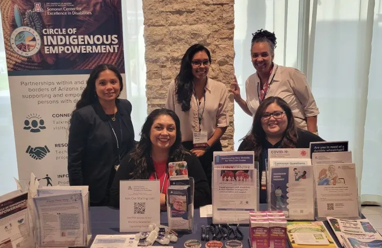 Sonoran Center staff Jacy Farkas, Celina Urquidez, Kelsey Montano, Lisa Ayo, and Jessica Rojas Franco behind a table with informational brochures about the Sonoran Center programs.