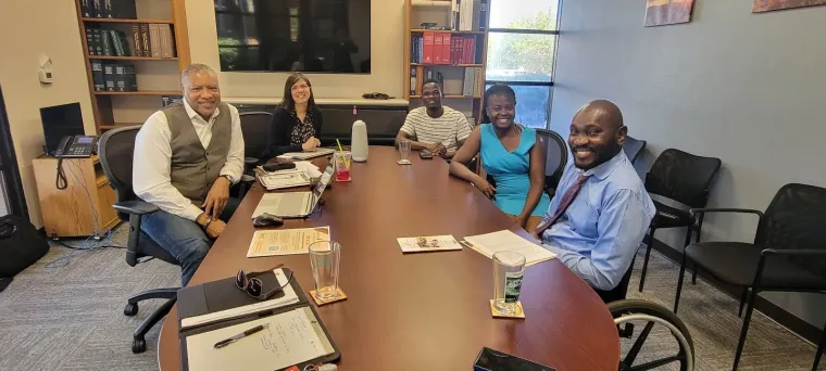 Denis meets with Renaldo Fowler (left) and Natalie Luna Rose (second from left) at the office of Disability Rights Arizona. All are seated indoors around a table, facing the camera and smiling.