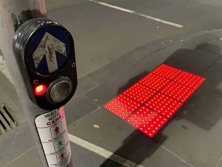 a crosswalk with a walk button and a textured tactile warning strip