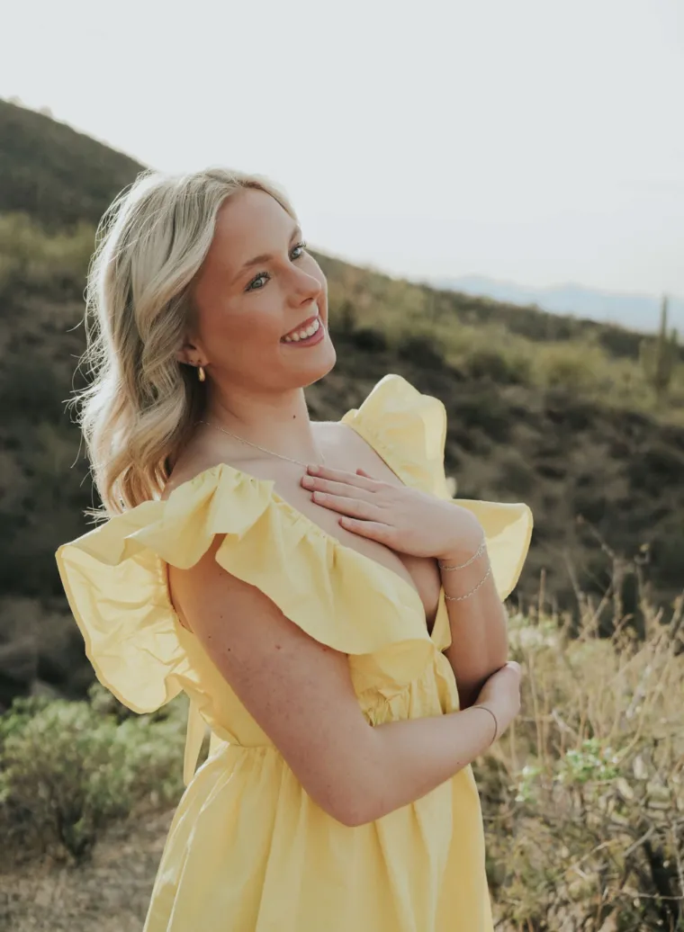 Photo of a woman wearing a yellow flowy dress with blonde shoulder length hair smiling 